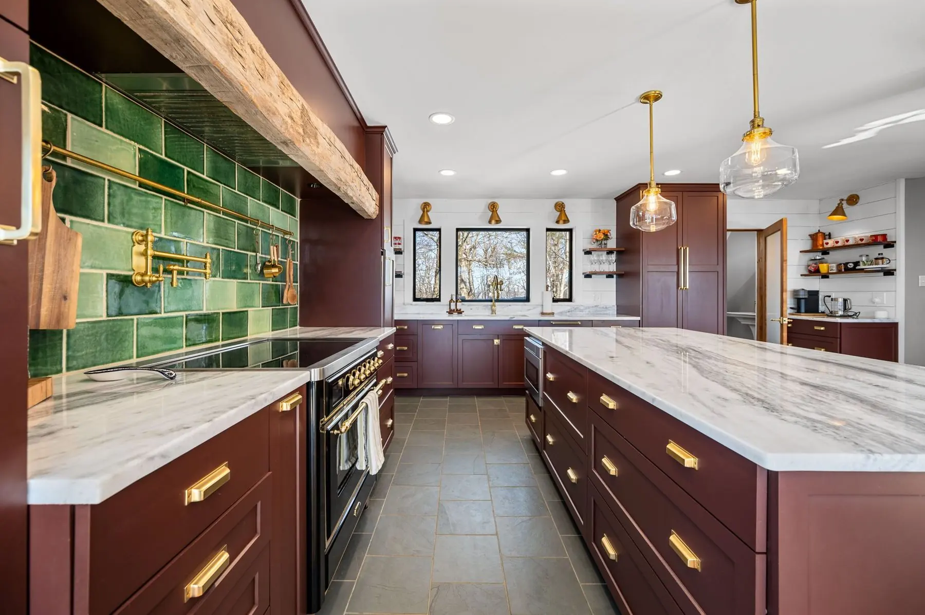 Burgundy kitchen with emerald tile, marble counters, brass fixtures, and a long island