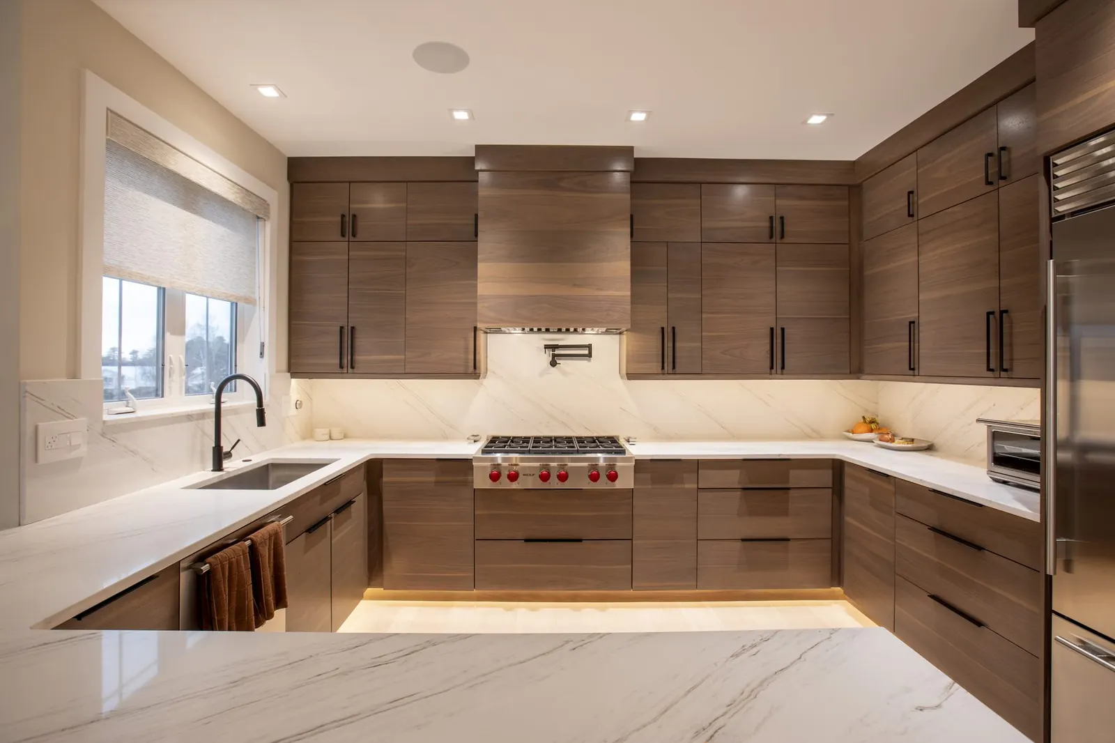 Walnut kitchen with marble counters, Wolf range, and a waterfall island, designed by Lacillade Kitchen + Bath