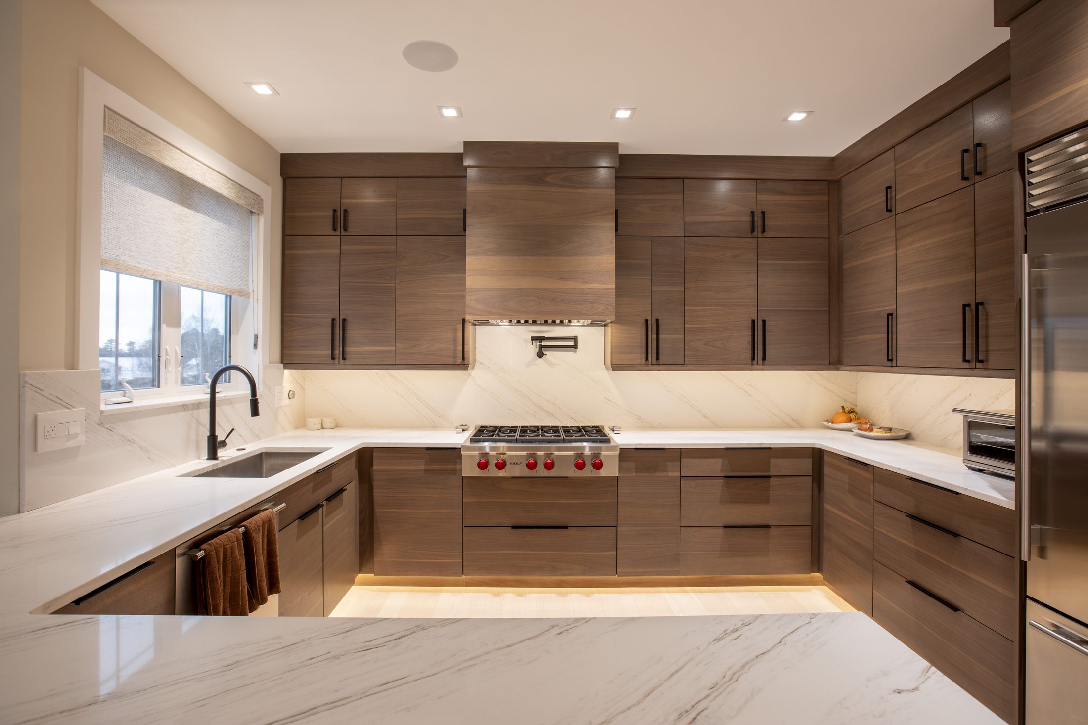Walnut kitchen with marble counters and a stainless Wolf range